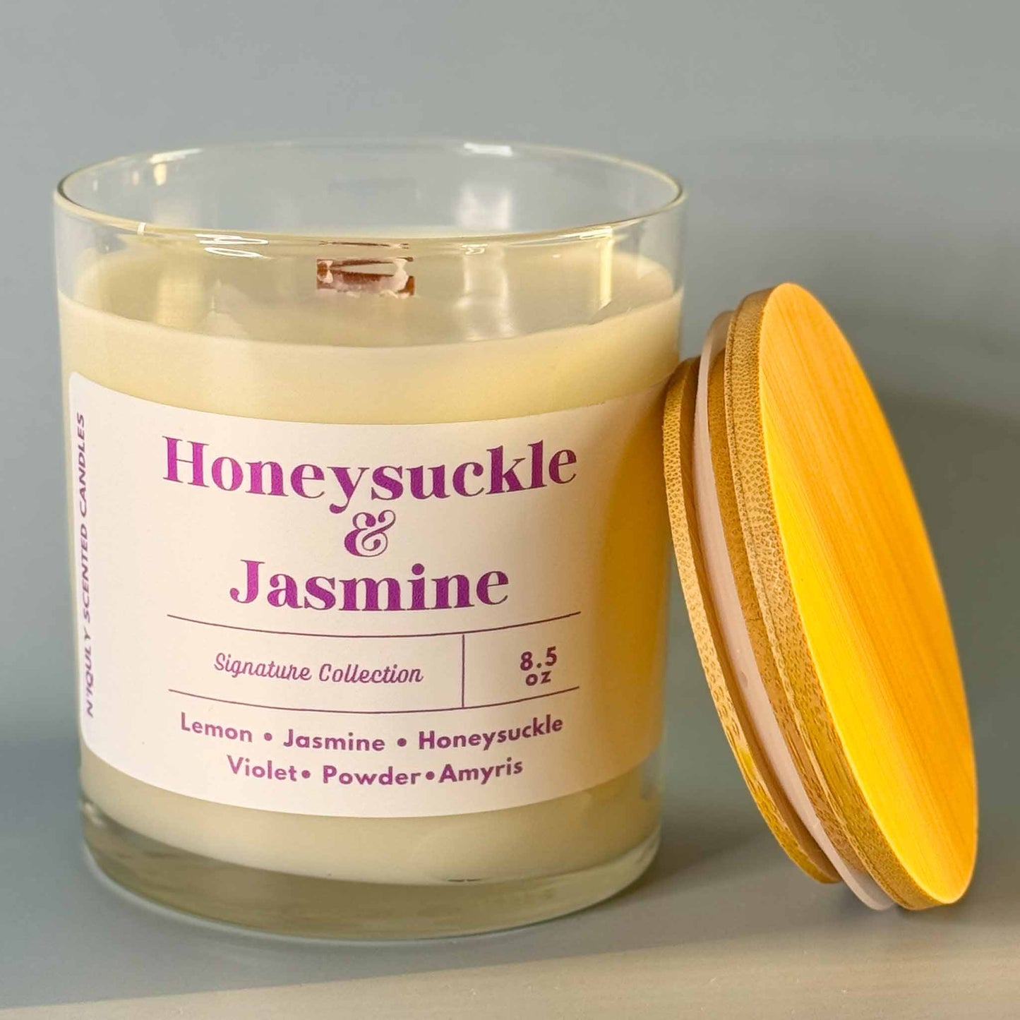 A glass jar candle labeled Honeysuckle & Jasmine, gently glowing.